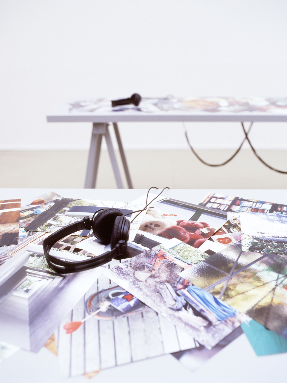 A close-up picture showing the top of one table in the PLOTS installation, which looks like it is printed with color photographs of a variety of everyday things. There are headphones on the table.